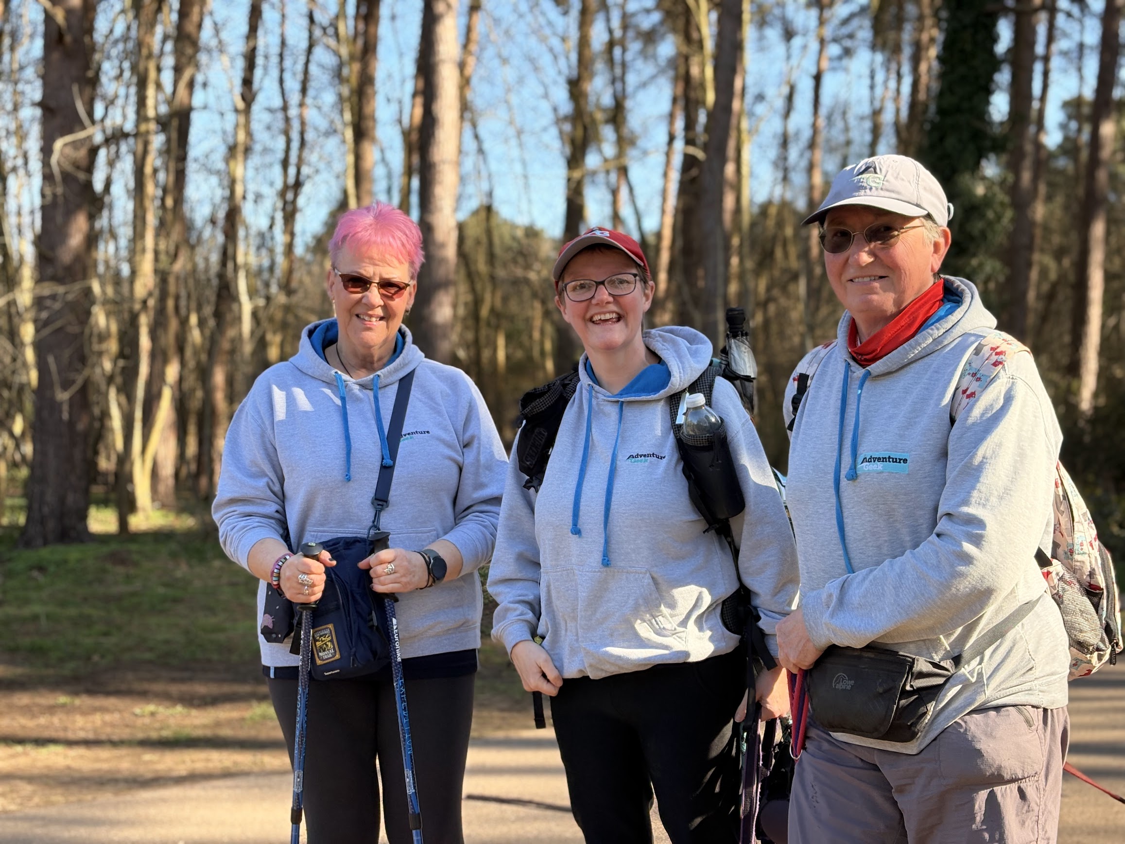 Three smiling Adventure Geek members wearing club hoodies during a woodland walk.